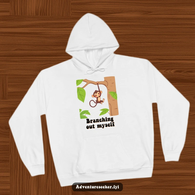 Funny hoodie showing a mischievous monkey character hanging casually from a thick jungle tree branch, embodying playful freedom.